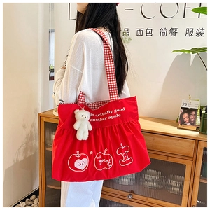 Detailed view of red canvas tote with white apple print and plush bear charm