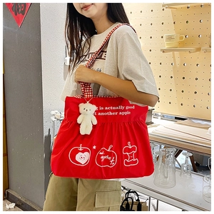Detail of red canvas tote bag with apple prints and a cute plush bear charm