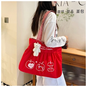 Detail of red canvas tote bag featuring cute teddy bear pendant and apple print design