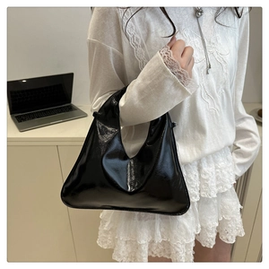 Dettaglio di una borsa hobo nera in vernice lucida con fibbie in metallo chic