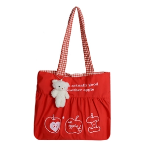 Red nylon tote bag with apple print and plush bear keychain on a white background