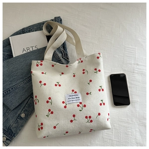 Detail of white corduroy tote bag with red cherry prints and woven straps on white fabric