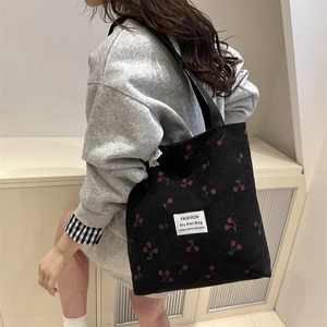 Black corduroy tote bag with red cherry prints and woven handles on a model