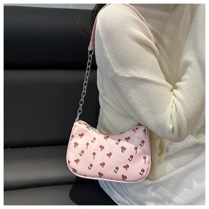 Sac à bandoulière rose avec motif cerise et détail de chaîne porté par un mannequin