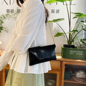 Fashionable black patent leather envelope crossbody bag with a gold chain strap
