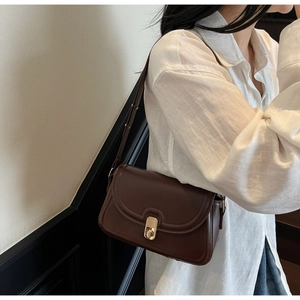 Détail d'un sac à bandoulière marron vintage avec fermoir doré porté par un modèle