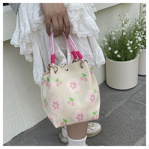 Close-up of the knitted floral bucket bag with cherry patterns and pink woven handles