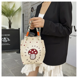 Detail of canvas bucket bag featuring mushroom illustration and woven rope handle strap