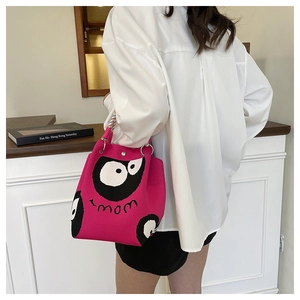 Close-up of pink knitted bucket bag with cartoon eyes and rainbow woven handle strap