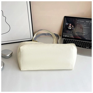 Detail of a large cream canvas tote bag with gray straps on a minimalist desk setup