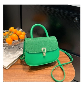Détail d'un sac à main en cuir vert et tissu pailleté sur une table en bois