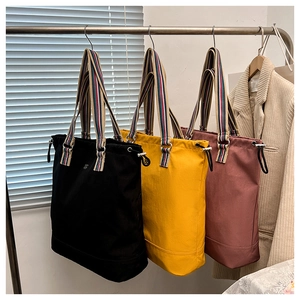Three minimalist canvas tote bags in black, yellow and red with colorful striped handles