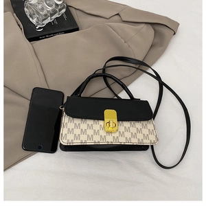 Detail of black crossbody bag with M-pattern print on beige blazer backdrop