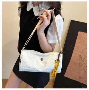 Détail d'un sac à bandoulière en tissu blanc avec sangle jaune et étiquette de marque