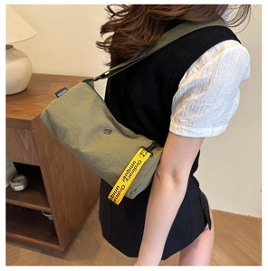 Détail du sac bandoulière en nylon vert olive avec sangle tissée jaune et étiquette
