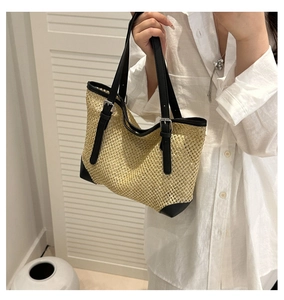 Detail of hand-woven straw tote with black leather trim and adjustable straps for summer