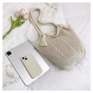 Detail of hand-woven beige crochet tote bag with cotton rope straps and tassel decor