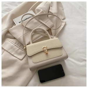 Detail of beige square bag with textured fabric, smooth leather and gold horseshoe buckle