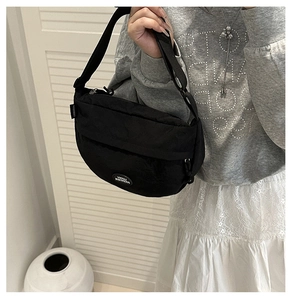 Detail of a black crescent crossbody bag with adjustable strap and brand logo patch