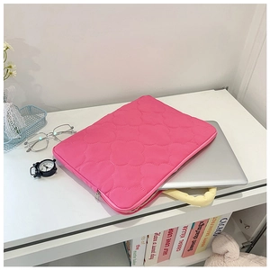 Detail of rose pink quilted laptop sleeve with floral stitching and handle on desk