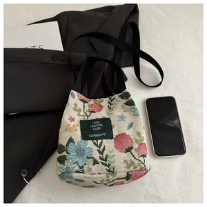 Detail of floral canvas bucket bag with woven handles and green logo patch