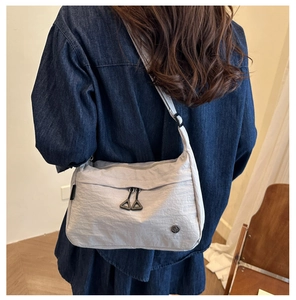 Detail of light gray nylon crossbody bag with black triangular zippers and adjustable strap