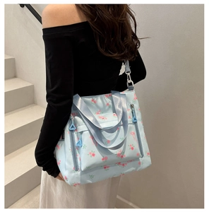 Detail of blue floral tote bag featuring functional front zippers and soft nylon fabric