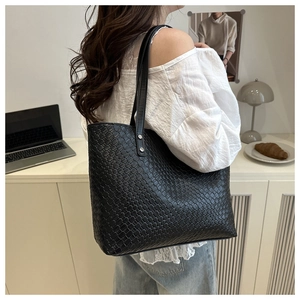 Detail of black woven leather tote bag showing checkerboard texture and sturdy handles