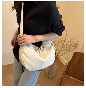 Detail of a beige canvas half-moon crossbody bag with a small round pouch and rope zippers