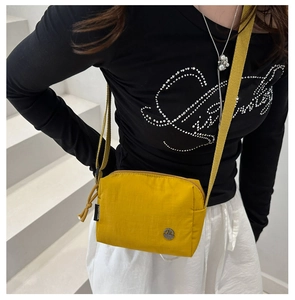Close-up of a yellow nylon crossbody bag featuring a woven strap and metal logo detail