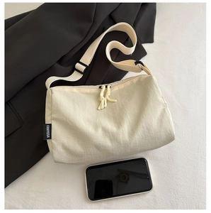 Détail du sac beige avec bandoulière réglable, étiquette latérale et tirette de zip