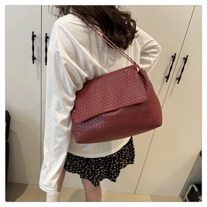 Detail of burgundy woven crossbody bag showing leather chain strap on shoulder