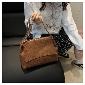 Detail of a brown woven texture flap handbag with a metallic chain strap on shoulder