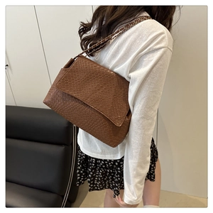Detail of a brown woven pattern crossbody bag with a metal chain strap on a model