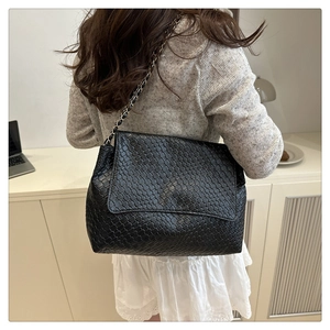 Detail showing a black woven leather shoulder bag with chain strap on a model back
