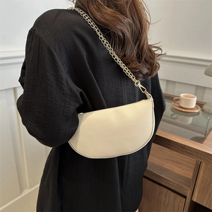 Minimalist beige half-moon shoulder bag with gold chain strap in chic daily setting