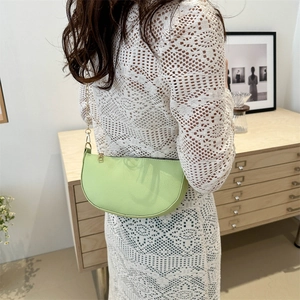 Pale green pebble leather crescent shoulder bag with gold chain strap on female model