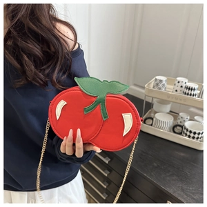 Close-up of creative cherry cross-body bag with golden chain and green leaf detail