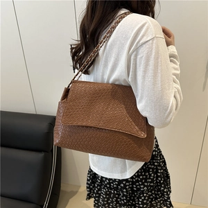Fashionable brown snakeskin texture crossbody bag with metal chain strap worn by a model