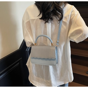 Detail of light blue crossbody bag featuring woven texture and round handle
