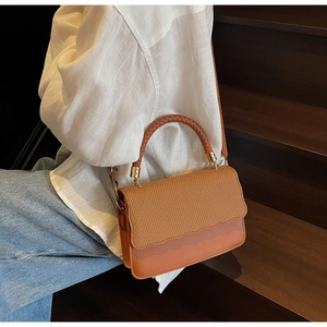 Detail of woven texture and wave edge flap on a brown retro shoulder bag with gold hardware