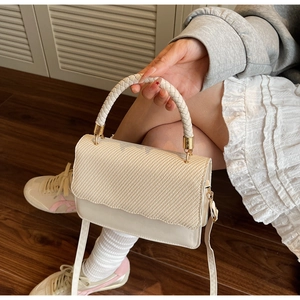 Macro detail of cream crossbody bag featuring woven handle and wavy flap edge design