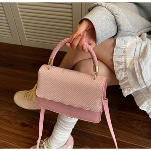 Detail of pink crossbody bag with woven texture flap and golden hardware accents