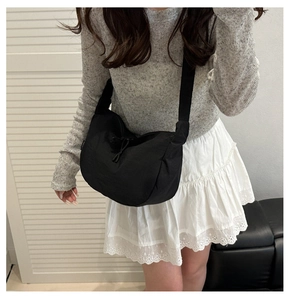 Detail of a black crescent nylon crossbody bag with decorative drawstrings and a wide strap