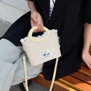 Sac bandoulière tissé beige avec bordure en dentelle et nœud tenu par un mannequin