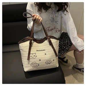 Close-up of woven straw tote bag featuring contrast leather handles and cat embroidery
