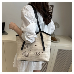 Detail of straw woven tote bag featuring cat embroidery and elegant black leather straps