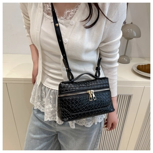 On-body shot of a black woven crossbody bag with adjustable strap and gold zippers