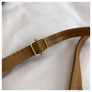 Detail of adjustable golden metal buckle and brown leather shoulder strap stitching