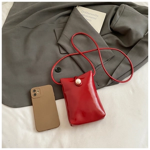 Détail macro du sac de téléphone en cuir verni rouge brillant avec un gros bouton perle